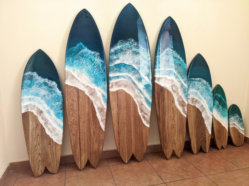 Op de afbeelding: Een set van zeven houten surfplank wanddecoraties met een blauw en wit hars ocean wave design. De surfplanken zijn gerangschikt in aflopende volgorde.