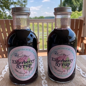 May include: Two glass bottles of elderberry syrup with silver lids. The bottles are labeled "Long Traditional Elderberry Syrup with Honey & Ginger" and contain 12 fl oz (355 ml).