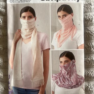 May include: Simplicity sewing pattern S9313 for one size face coverings. The envelope displays three variations: a long beige scarf with fringe, a solid light pink triangular bandana, and a patterned pink and white neck gaiter style covering.