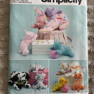 May include: Simplicity sewing pattern R11932 featuring illustrations of various stuffed animals including a pink pig with sprinkles, a blue rabbit, a dalmatian dog, and several cats in yellow, orange, and white with orange stripes, all labeled with letters.