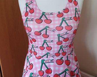 May include: A pink and white gingham sleeveless dress with a cherry print. The cherries are red with green stems and leaves. The dress has the word "cutie" written on a banner on each cherry.