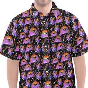 Peut inclure: Une chemise à manches courtes à boutons avec un fond noir et un motif répété de personnages de dessins animés violets, orange et bleus. Les personnages tiennent des pinceaux et des éclaboussures de peinture sont visibles sur la chemise.
