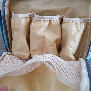 May include: The inside of a light blue diaper bag with a beige lining. The bag has three zippered pockets and a mesh pocket.