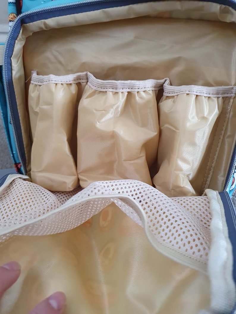 May include: The inside of a light blue diaper bag with a beige lining. The bag has three zippered pockets and a mesh pocket.