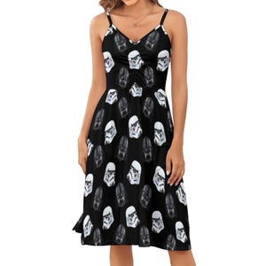 May include: Black spaghetti strap dress featuring a repeating pattern of white Stormtrooper and black Darth Vader helmet graphics. The dress has a V-neckline and a flared skirt, perfect for a casual or themed event.