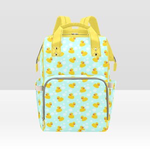 May include: A light blue and yellow diaper bag with a pattern of yellow rubber ducks on a light blue background. The bag has a large main compartment, two side pockets, and a top handle.