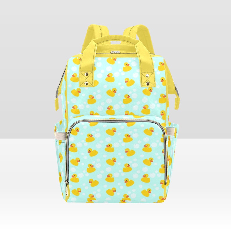 May include: A light blue and yellow diaper bag with a pattern of yellow rubber ducks on a light blue background. The bag has a large main compartment, two side pockets, and a top handle.