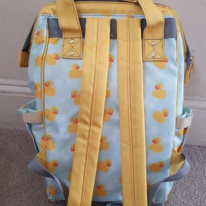 May include: A yellow and blue backpack with a rubber ducky pattern. The backpack has adjustable straps and a zippered front pocket.