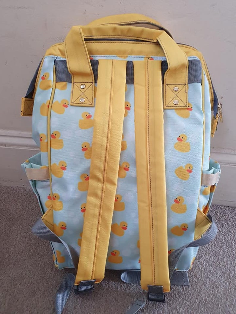 May include: A yellow and blue backpack with a rubber ducky pattern. The backpack has adjustable straps and a zippered front pocket.