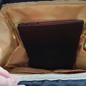 May include: A black backpack with a beige lining. A laptop computer is inside the backpack.