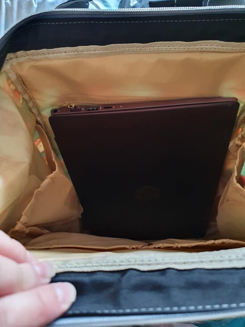 May include: A black backpack with a beige lining. A laptop computer is inside the backpack.