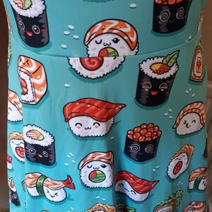 May include: A turquoise blue fabric with a repeating pattern of various types of sushi. The sushi is illustrated with cartoon faces and is in various colors, including red, orange, yellow, green, and black.