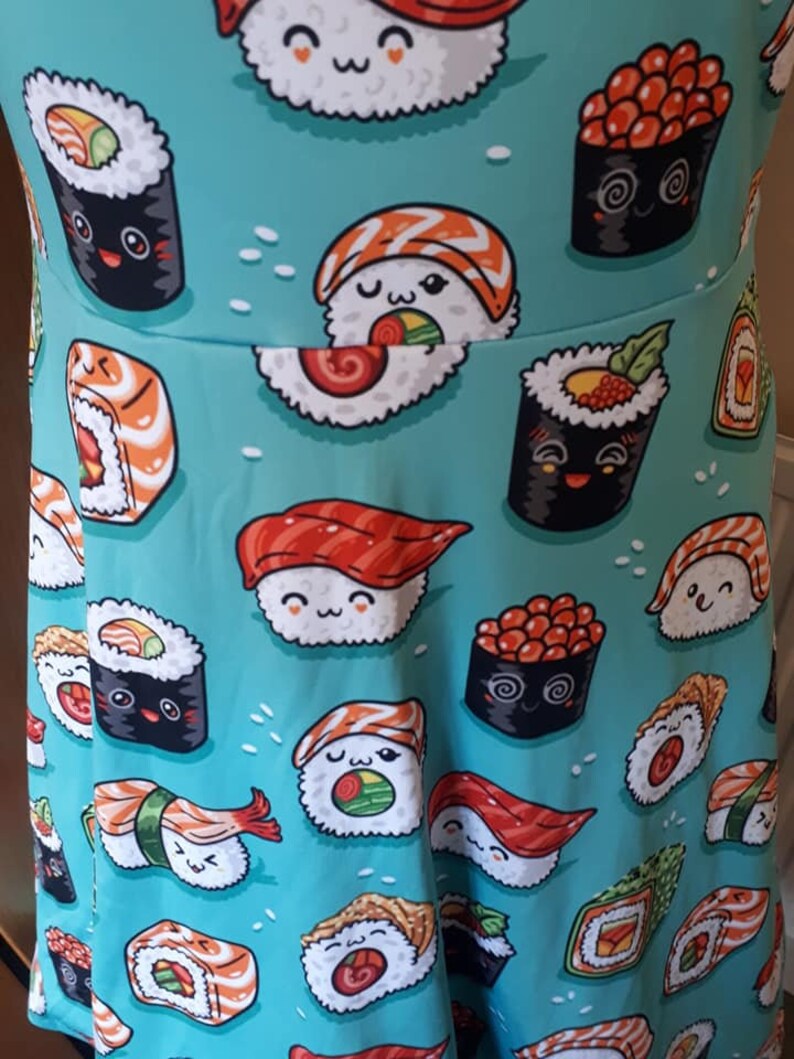 May include: A turquoise blue fabric with a repeating pattern of various types of sushi. The sushi is illustrated with cartoon faces and is in various colors, including red, orange, yellow, green, and black.