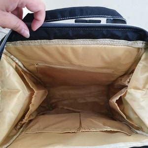 May include: The inside of a black backpack with a beige lining. The backpack has multiple pockets and compartments.