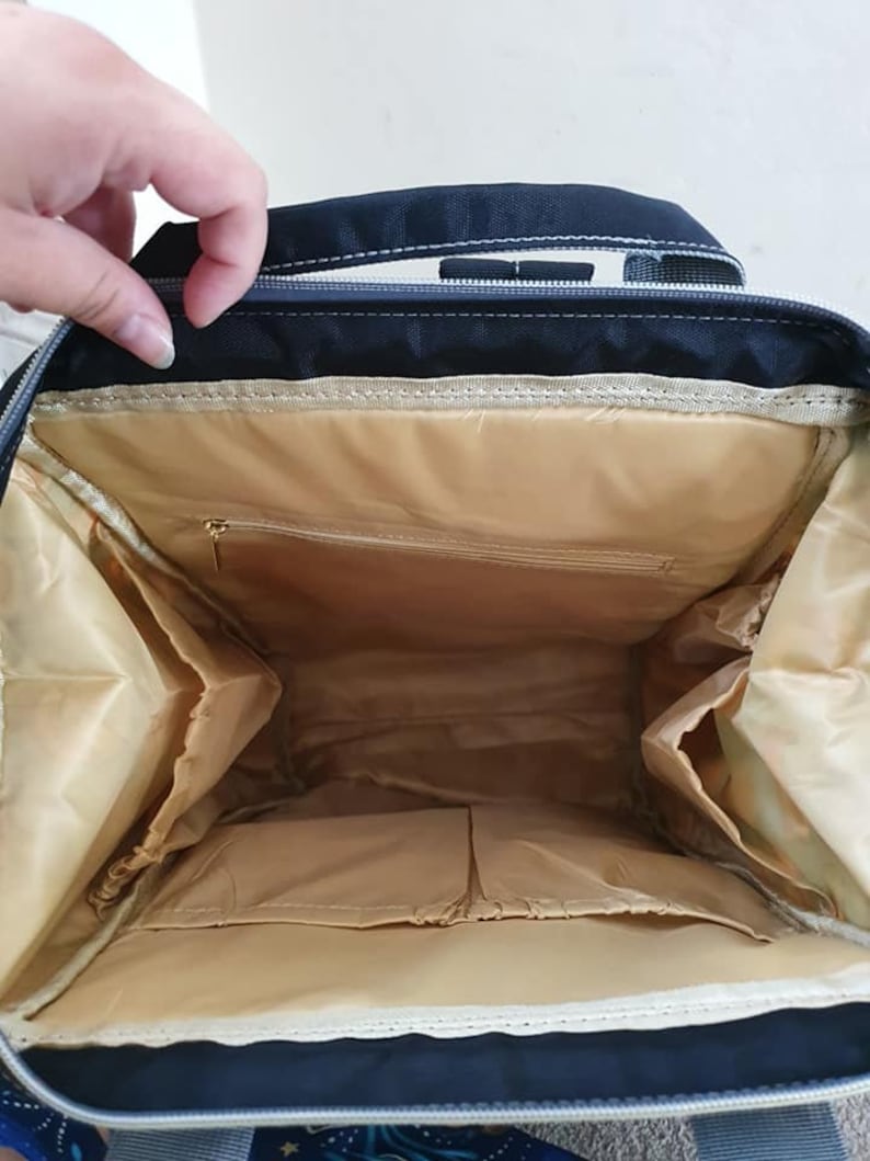 May include: The inside of a black backpack with a beige lining. The backpack has multiple pockets and compartments.