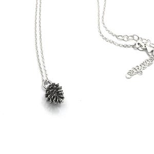 Può includere: Una collana con catena d'argento con un piccolo ciondolo a forma di pigna dettagliato.