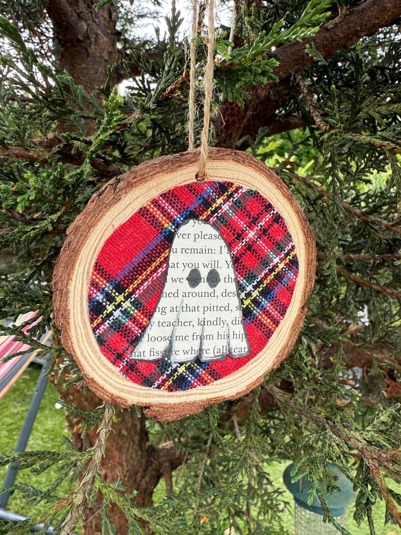 K&ouml;nnte beinhalten: Runder Weihnachtsbaumschmuck aus Holz mit rotem und schwarzem Karomuster. Der Schmuck hat eine ausgeschnittene Silhouette, mit Text darin. Er h&auml;ngt an einer Schnur aus Naturfaser.