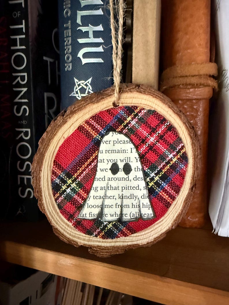 K&ouml;nnte beinhalten: Ein runder Holzschmuck mit einem rot-schwarz-gelben Karomuster. In der Mitte befindet sich ein Ausschnitt mit Text aus einem Buch. Der Schmuck wird an einer nat&uuml;rlichen Schnur aufgeh&auml;ngt, ideal f&uuml;r Feiertagsdekorationen.