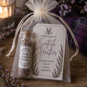 May include: A small glass vial filled with dried purple heather flowers, sealed with a cork, inside a sheer white organza drawstring bag. A rectangular paper tag is attached, featuring the text A little piece of Scottish Heather.