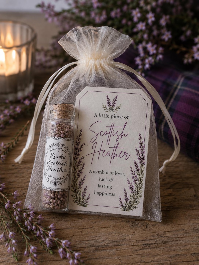 May include: A small glass vial filled with dried purple heather flowers, sealed with a cork, inside a sheer white organza drawstring bag. A rectangular paper tag is attached, featuring the text A little piece of Scottish Heather.