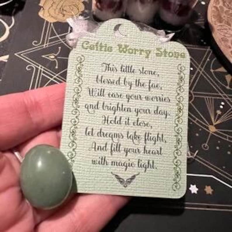 May include: A smooth, oval-shaped green aventurine worry stone paired with a light green rectangular card. The card features a crescent moon icon and the text: Celtic Worry Stone, This little stone, blessed by the fae, Will ease your worries and brighten your day. Hold it close, let dreams take flight, And fill your heart with magic light.