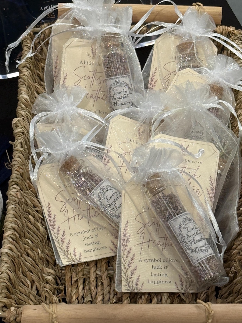 May include: Several small glass vials filled with dried purple heather, each sealed with a cork stopper and tucked into a white organza drawstring bag. Each bag includes a beige paper tag printed with the text A little piece of Scottish Heather.