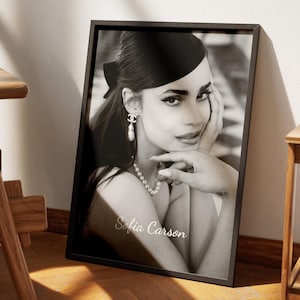 May include: Black and white framed portrait of Sofia Carson. The image shows a woman with dark hair, wearing a pearl necklace and earrings. The frame is black, and the text "Sofia Carson" is written in cursive at the bottom.