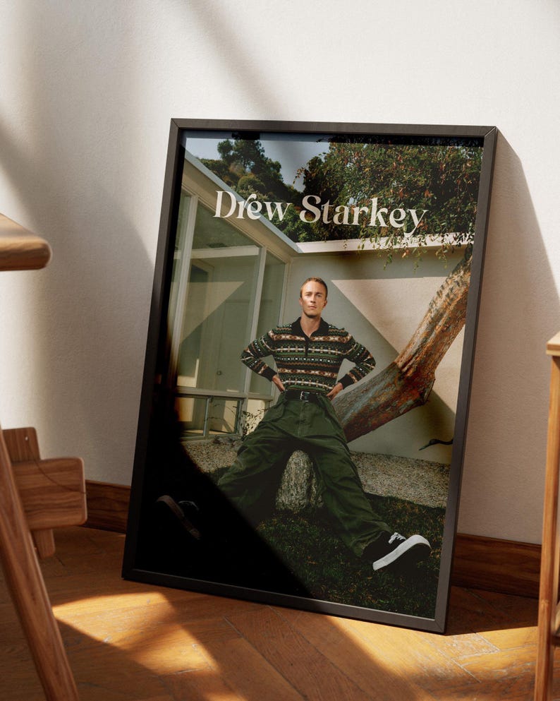 May include: Framed print with the text "Drew Starkey." The image depicts a person in a patterned sweater, green trousers, and black and white trainers. The background includes a house and a tree.