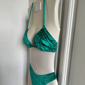 May include: Teal green velvet bikini top and bottom. The top is a triangle style with thin straps. The bottom is a high-cut style with a small amount of fabric covering the rear.