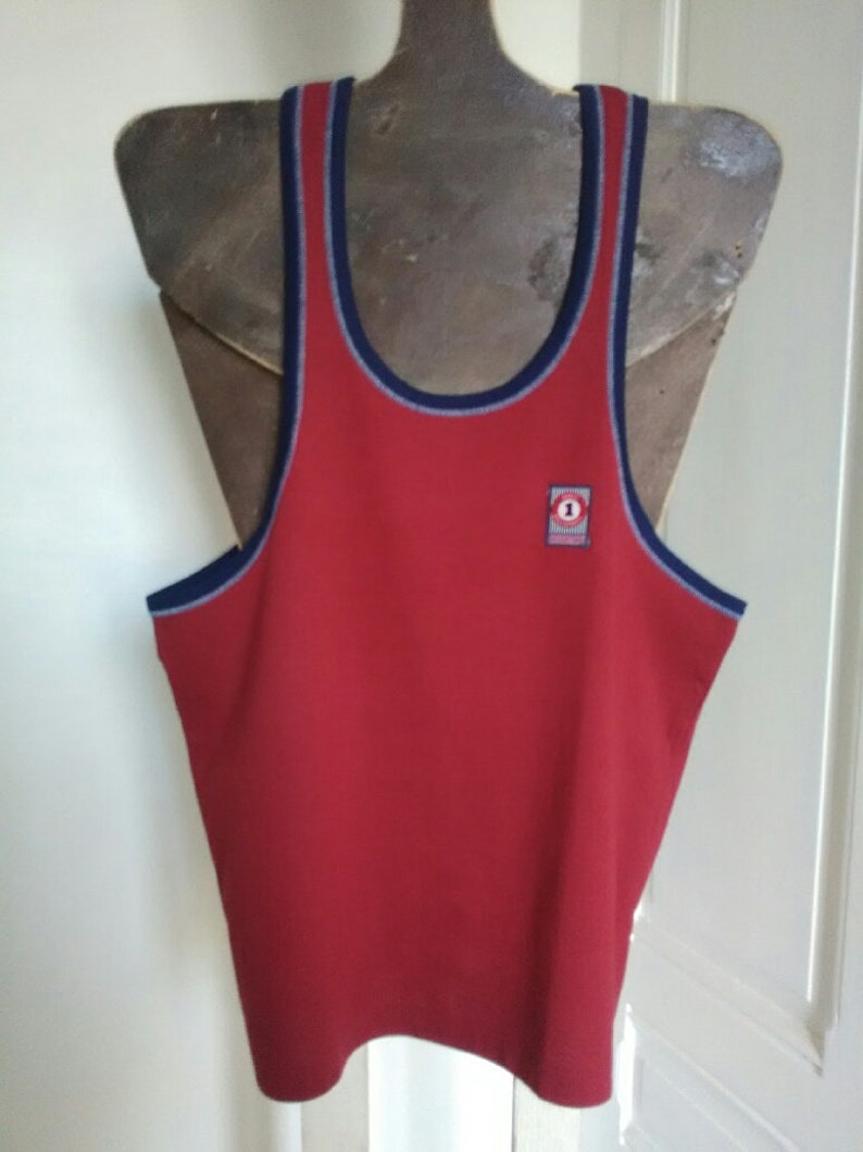 May include: Red sleeveless tank top with a blue and white trim around the neck and armholes. A small red and white logo with the number "1" is on the front of the shirt.