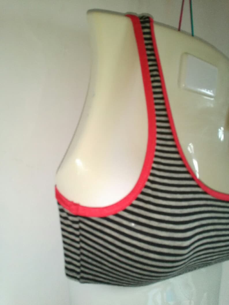 May include: A black and white striped sports bra with a red trim. The bra is on a white mannequin.