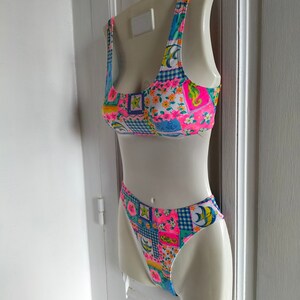Puede incluir: Un traje de ba&ntilde;o de dos piezas con un dise&ntilde;o de patchwork vibrante. La parte superior e inferior presentan una mezcla de estampados florales, cuadros y geom&eacute;tricos en rosa, azul, amarillo y verde. El traje de ba&ntilde;o se exhibe en un maniqu&iacute; blanco.