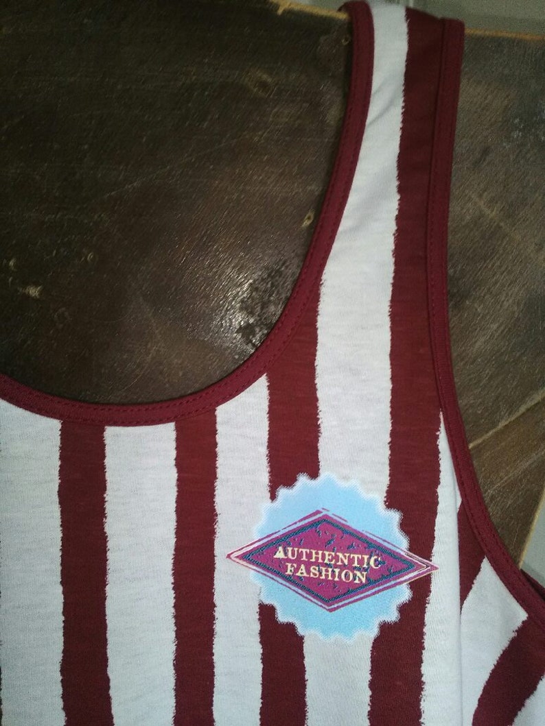 May include: A white and maroon striped tank top with a diamond-shaped patch that says "AUTHENTIC FASHION" in gold lettering.