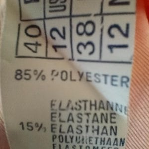 Pode incluir: Close-up de uma etiqueta de roupa com informa&ccedil;&otilde;es de tamanho e composi&ccedil;&atilde;o do tecido. A etiqueta mostra tamanhos para Fran&ccedil;a (40), US/UK (12), Alemanha (38) e Pa&iacute;ses Baixos (12). Lista 85% poli&eacute;ster e 15% elastano. A etiqueta &eacute; marcada "Made in France."
