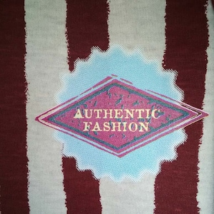 May include: A white and maroon striped fabric with a diamond-shaped patch that says "AUTHENTIC FASHION" in a white font with a pink background.