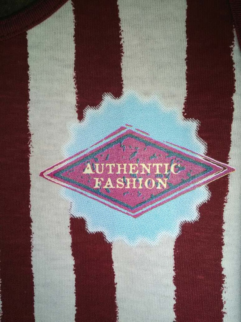May include: A white and maroon striped fabric with a diamond-shaped patch that says "AUTHENTIC FASHION" in a white font with a pink background.