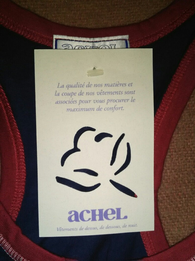 May include: A white tag with black text and a black graphic. The tag reads "La qualit&eacute; de nos mati&egrave;res et la coupe de nos v&ecirc;tements sont associ&eacute;es pour vous procurer le maximum de confort. achel V&ecirc;tements de dessus, de dessous, de nuit."