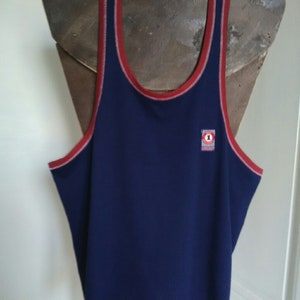 May include: A navy blue sleeveless shirt with red and white trim around the neck and armholes. The shirt has a small logo on the front with a red circle and the number "1" inside.