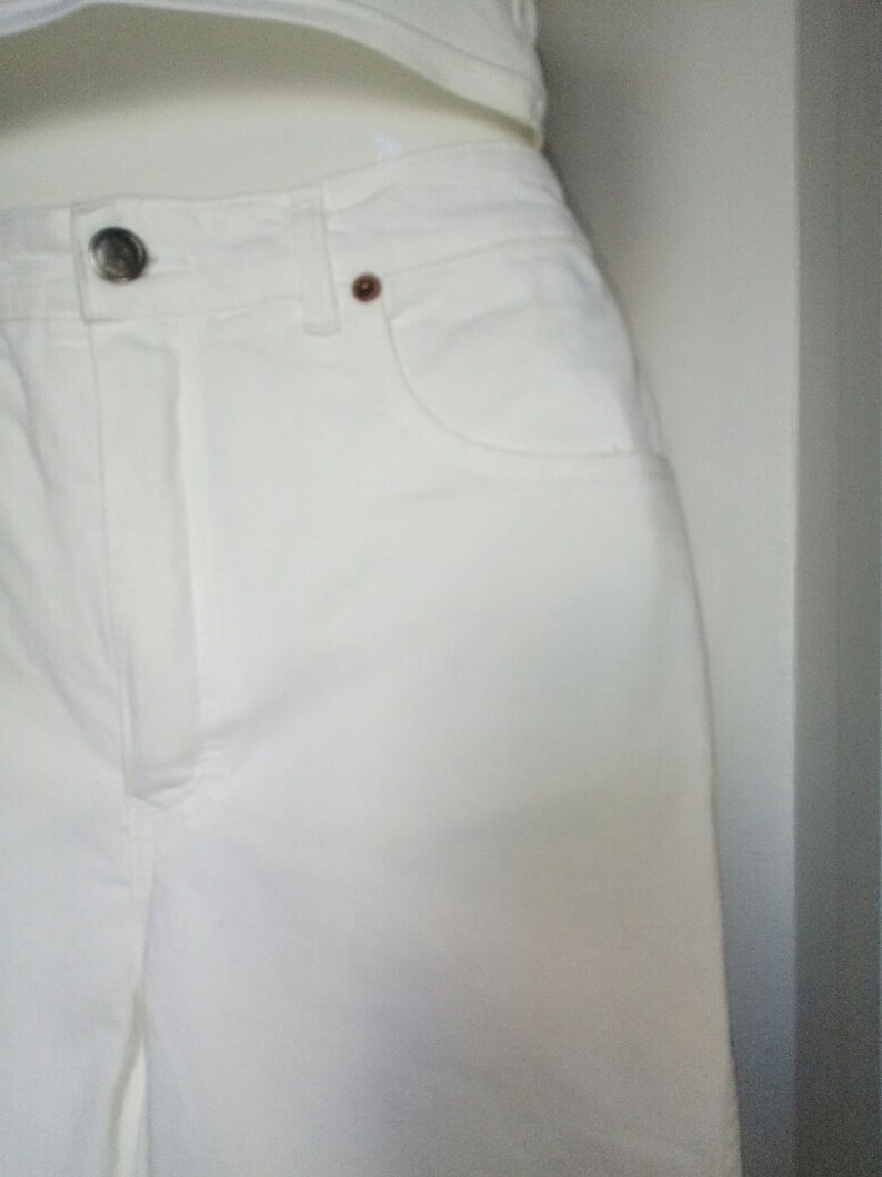 May include: White denim pants with a button fly and a front pocket.