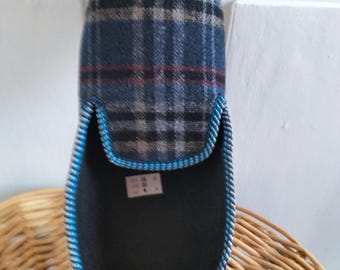 Puede incluir: Una zapatilla de casa con un patrón de cuadros azul, negro y rojo en la parte superior. El interior está forrado con tela negra y la abertura está ribeteada con un vivo texturizado azul y blanco. Se ve una pequeña etiqueta blanca.