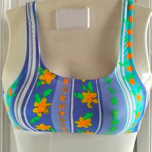 Op de afbeelding: Een blauw en wit gestreept badpak bovenstuk met een bloemenpatroon. De bloemen zijn oranje, geel en groen.