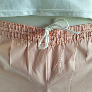 Puede incluir: Pantalones cortos de color melocot&oacute;n con cord&oacute;n blanco y costuras naranjas alrededor de la cintura.
