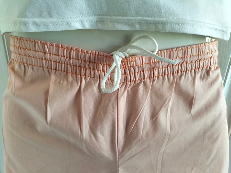 Puede incluir: Pantalones cortos de color melocot&oacute;n con cord&oacute;n blanco y costuras naranjas alrededor de la cintura.