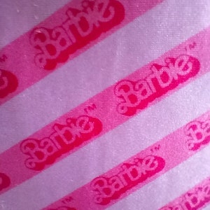 Puede incluir: Tela de rayas rosa y blanca con la palabra "Barbie" repetida en letras rosas.