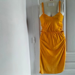 May include: A mustard yellow sleeveless dress with a fitted bodice and a flowing skirt. The dress has a scoop neckline and a gathered waist.