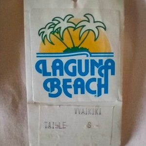 Puede incluir: Etiqueta blanca con un logotipo azul y amarillo que dice "Laguna Beach" y "Waikiki". La etiqueta tambi&eacute;n dice "Taille 6".