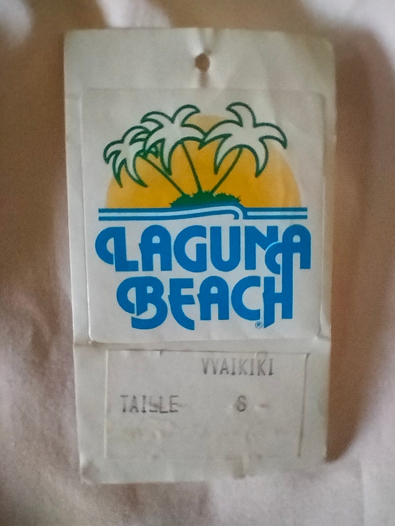 Puede incluir: Etiqueta blanca con un logotipo azul y amarillo que dice "Laguna Beach" y "Waikiki". La etiqueta tambi&eacute;n dice "Taille 6".