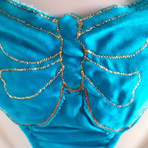 May include: A turquoise blue fabric with a gold butterfly design. The butterfly is outlined in gold thread.