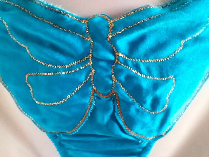May include: A turquoise blue fabric with a gold butterfly design. The butterfly is outlined in gold thread.