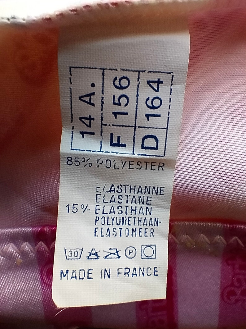 Puede incluir: Una etiqueta blanca con texto azul que indica las tallas 14A, F 156 y D 164. La etiqueta tambi&eacute;n indica 85% poli&eacute;ster y 15% elastano, poliuretano-elast&oacute;mero. La etiqueta incluye instrucciones de cuidado con un s&iacute;mbolo de lavado a 30 grados Celsius, un tri&aacute;ngulo con una X en su interior, un c&iacute;rculo con una P en su interior y un c&iacute;rculo con una l&iacute;nea que lo atraviesa. La etiqueta tambi&eacute;n indica "Hecho en Francia".